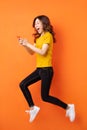 Young asian girl using the phone and jumping on orange background Royalty Free Stock Photo