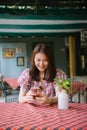 Young asian girl using smartphone waiting for her friend to come at restaurant. Royalty Free Stock Photo