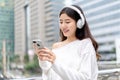 Young Asian girl wearing headphones listening to music from mobile phone