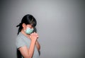 A young Asian girl wearing a mask to prevent PM2.5 and COVID-19 is at home, praying to God, worshiping on the day of the coronavir Royalty Free Stock Photo