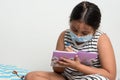 Young Asian girl wearing protective face mask sitting on her bed writing in a diary. Royalty Free Stock Photo