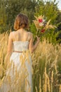 A young Asian girl in a white dress walking in a field with fluffy ears. A model from back with a short haircut and wildflowers. Royalty Free Stock Photo