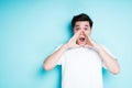 Young asian guy puts his hands around his mouth and opens it in surprise while standing against a bright background Royalty Free Stock Photo