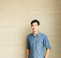 Young asian handsome man who is wearing a blue shirt casual wear is standing in front of wooden wall in office  morning time. Royalty Free Stock Photo