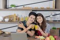 Young Asian healthy couple with casual clothes is smiling and holding fresh orange juice in kitchen room at home in holiday. Royalty Free Stock Photo