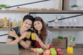 Young Asian healthy couple with casual clothes is smiling and holding fresh orange juice in kitchen room at home in holiday. Royalty Free Stock Photo