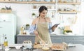 Young Asian housewife in kitchen using tablet for searching recipes online cooking the bakery dough homemade Royalty Free Stock Photo