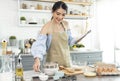 Young Asian housewife in kitchen using tablet for searching recipes online cooking the bakery dough homemade Royalty Free Stock Photo