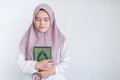 Young Asian Islam woman wearing headscarf is holding holy al quran with close eyes and calm face. Indonesian woman on gray Royalty Free Stock Photo