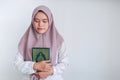 Young Asian Islam woman wearing headscarf is holding holy al quran with close eyes and calm face. Indonesian woman on gray Royalty Free Stock Photo