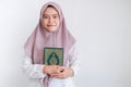 Young Asian Islam woman wearing headscarf is holding holy al quran in hand with smile and happy face. Indonesian woman on gray Royalty Free Stock Photo