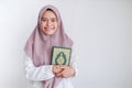 Young Asian Islam woman wearing headscarf is holding holy al quran in hand with smile and happy face. Indonesian woman on gray Royalty Free Stock Photo