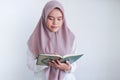 Young Asian Islam woman wearing headscarf is praying or read Quran - the holy book of Islam with smile and serious face. Royalty Free Stock Photo