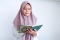 Young Asian Islam woman wearing headscarf is praying or read Quran - the holy book of Islam with smile and serious face. Royalty Free Stock Photo