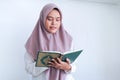 Young Asian Islam woman wearing headscarf is praying or read Quran - the holy book of Islam with smile and serious face. Royalty Free Stock Photo