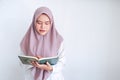 Young Asian Islam woman wearing headscarf is praying or read Quran - the holy book of Islam with smile and serious face. Royalty Free Stock Photo