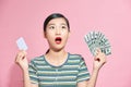 Young asian lady holding credit card and fan of money, posing isolated over pink studio background, girl doing shopping online Royalty Free Stock Photo