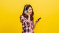 Young Asian lady wearing wireless headphones listening to music from smartphone with cheerful expression. Royalty Free Stock Photo