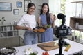 Young Asian lesbian couple blogger influencer vlogger shooting video in kitchen. LGBT couple live- streaming cooking class from ho Royalty Free Stock Photo