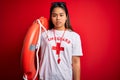 Young asian lifeguard girl wearing t-shirt with red cross using whistle holding orange float with a confident expression on smart