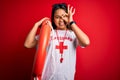 Young asian lifeguard girl wearing t-shirt with red cross using whistle holding orange float with happy face smiling doing ok sign