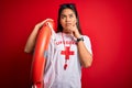 Young asian lifeguard girl wearing t-shirt with red cross using whistle holding orange float serious face thinking about question,