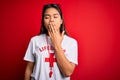 Young asian lifeguard girl wearing t-shirt with red cross using whistle over isolated background bored yawning tired covering
