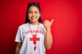 Young asian lifeguard girl wearing t-shirt with red cross using whistle over isolated background Pointing to the back behind with