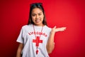 Young asian lifeguard girl wearing t-shirt with red cross using whistle over isolated background smiling cheerful presenting and