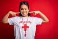 Young asian lifeguard girl wearing t-shirt with red cross using whistle over isolated background smiling cheerful showing and