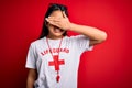 Young asian lifeguard girl wearing t-shirt with red cross using whistle over isolated background smiling and laughing with hand on
