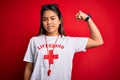 Young asian lifeguard girl wearing t-shirt with red cross using whistle over isolated background Strong person showing arm muscle,