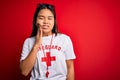 Young asian lifeguard girl wearing t-shirt with red cross using whistle over isolated background touching mouth with hand with
