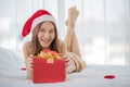 A young asian long brown hair female wearing red and white santa hat lying down on white sheet bed crossing her legs open cover of Royalty Free Stock Photo