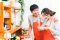 Young Asian lovely couple cooking together at home kitchen, wear red apron making lunch meal. Girl taste soup using spoon