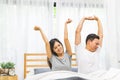 Young Asian lovely married couple wake up stretching together on bed in bedroom. Morning rise and shine, lazy day