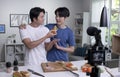 Young Asian male couple blogger influencer vlogger shooting video in kitchen. LGBT gay couple live- streaming cooking class Royalty Free Stock Photo