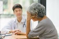 Young Asian male doctor holding hands with a senior patient woman, offering hope and kindness at a modern clinic office. Royalty Free Stock Photo