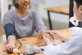 Young Asian male doctor holding hands with a senior patient woman, offering hope and kindness at a modern clinic office. Royalty Free Stock Photo