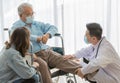 A young asian male doctor wearing white lab coat and face mask checking left knee of old fat gray hair patient wearing light blue Royalty Free Stock Photo