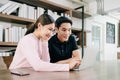 Young Asian male and female wearing pink sweater working together on the wooden table with laptop. Royalty Free Stock Photo