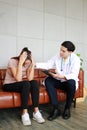 Young asian male psychiatrist is specialist in psychiatry is touching shoulder on Caucasian female Patient is headache on sofa.