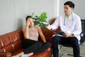 Young asian male psychiatrist is specialist in psychiatry is touching shoulder on Caucasian female Patient is headache on sofa and