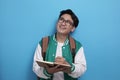 Young Asian male student wearing green baseball jacket writing on book and thinking Royalty Free Stock Photo