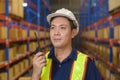 Young asian male worker wearing helmet using talki walki in modern warehouse