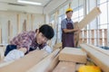 Young asian male worker wearing plaid shirt and blue jean apron with white gloves holding saw cutting wood stick on the table full Royalty Free Stock Photo