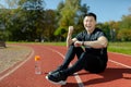 A young Asian man, an athlete sitting on a stadium treadmill. He looks at the smartwatch, fitness bracelet. Shows a Royalty Free Stock Photo