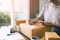 Young asian man business owner hands writing address on cardboard box at workplace or home office