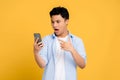 Young Asian man in casual clothes is shocked by something on his smartphone. Yellow background isolated