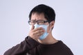 Young Asian man is coughing, feeling unwell, vomit sick with wearing a medical blue face mask isolated on white background, close Royalty Free Stock Photo